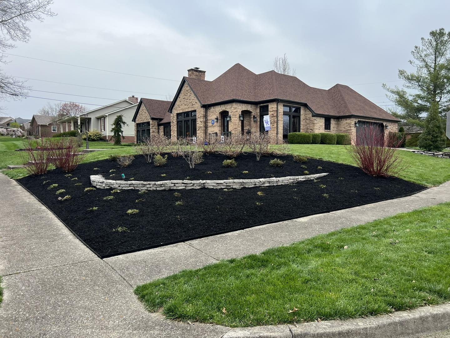 A freshly mulched front yard with a stone accent wall and shrubs