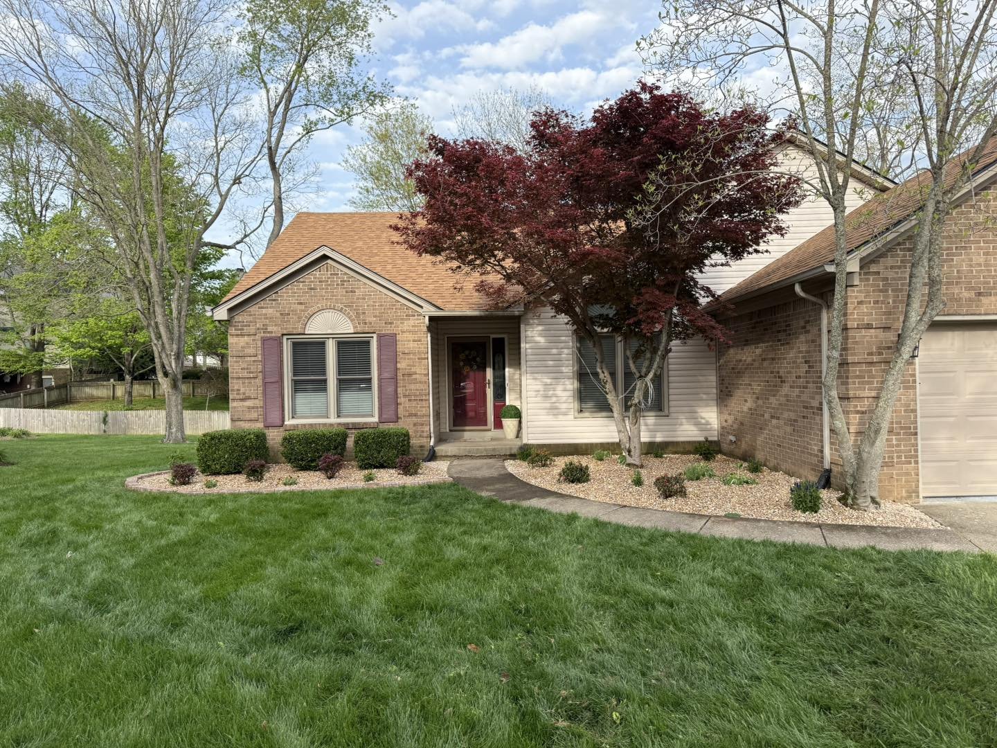 A neatly maintained cottage-style home with a red maple tree and tidy beds