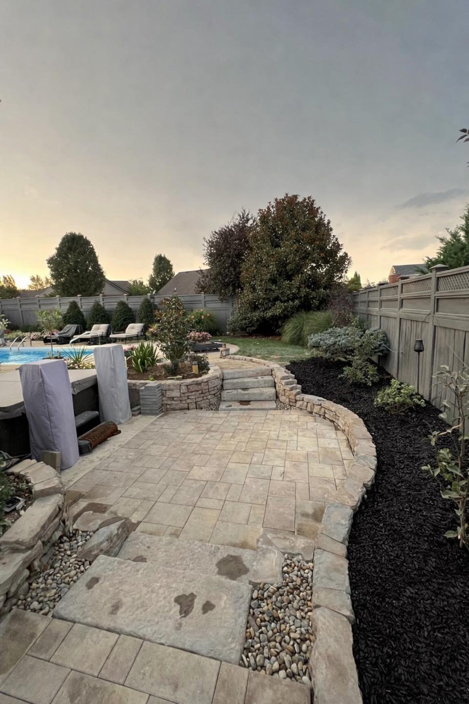 A custom paver patio with stone retaining wall built around a pool at sunset